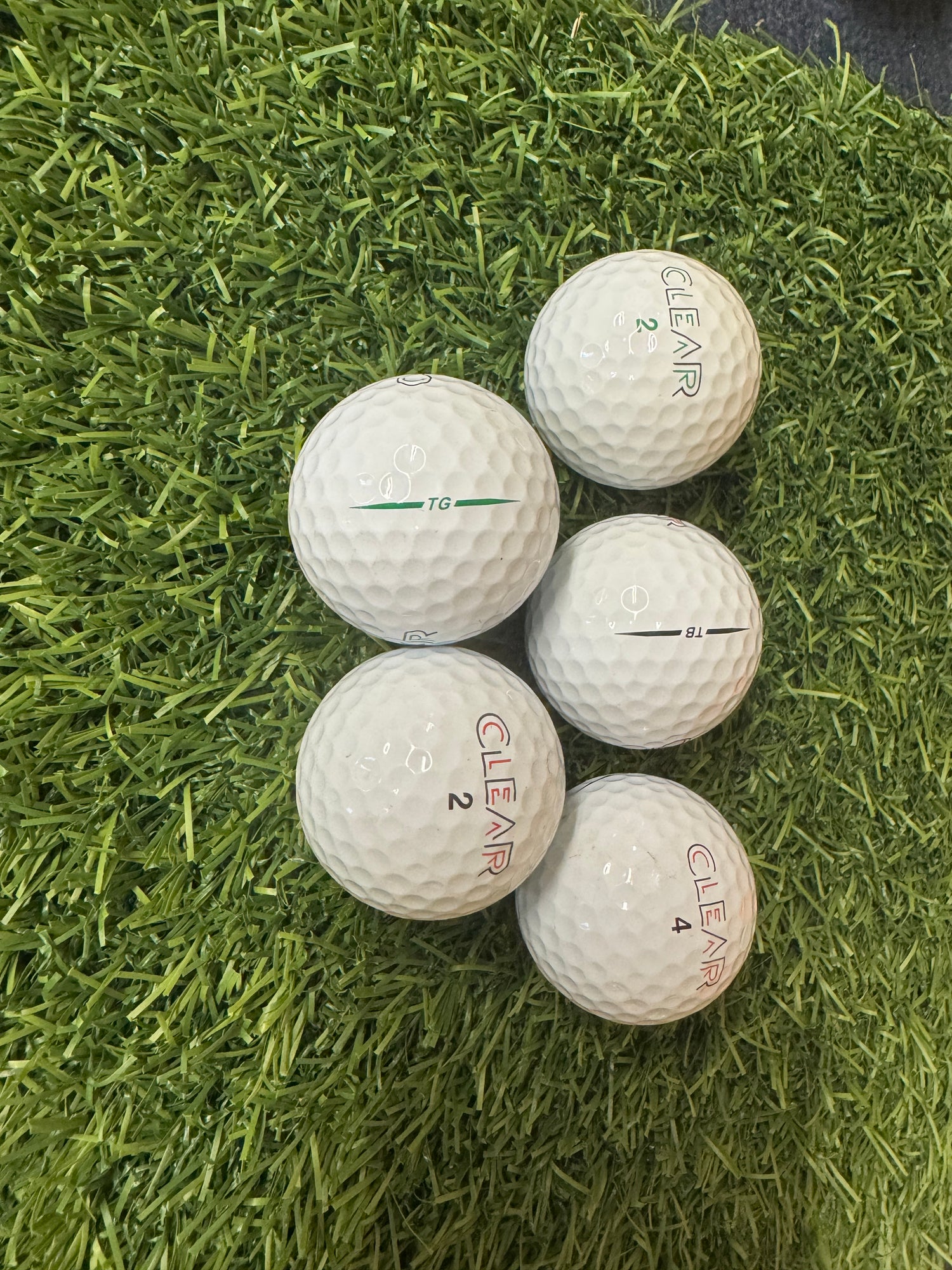 Five golf balls with 'Clear' branding on a grass surface