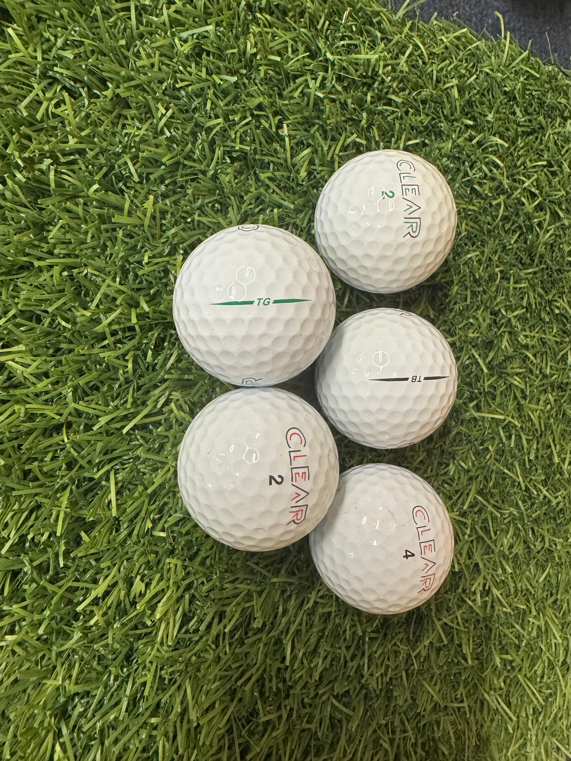 Five golf balls with 'Clear' branding on a grass surface